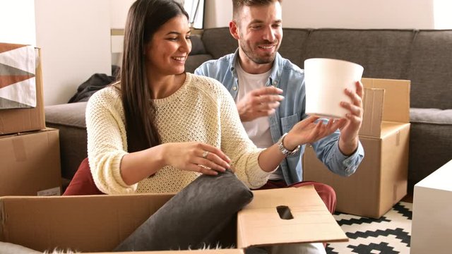 Smiling young couple move into a new home sitting on floor and unpacking.
