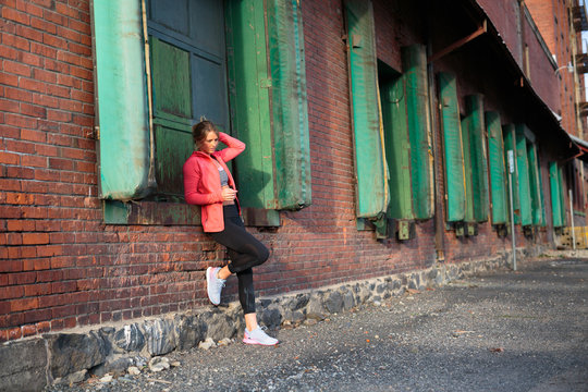 A fit, blonde woman wearing athletic attire poses for a portrait near an old brick warehouse in downtown Spokane, Washington.