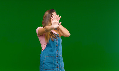 young pretty woman covering face with hand and putting other hand up front to stop camera, refusing...