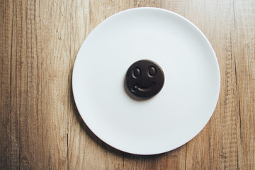 Chocolate cookies with a smiling face, smile, lie on a white plate standing on a wooden table. place for the inscription.