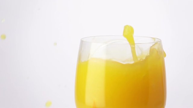 Slice of Orange Falling into a Glass of Orange Juice, Splashing Drops. Slow Motion.