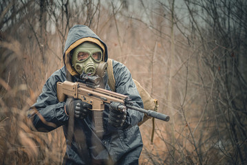 Fototapeta premium Soldier with airsoft rifle in raincoat and gas mask outdoor.