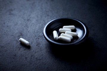 Arginine capsules. Bodybuilding food supplements on dark stone background. Close up.