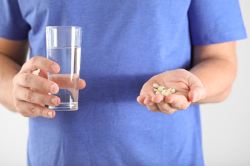 Man with pills on light background, closeup