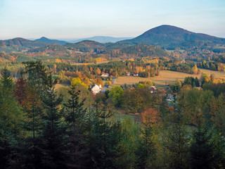 Aerial view from on small village Travnik in luzicke hory, Lusatian Mountains with autumn colored deciduous and coniferous tree forest and green hills in golden hour light