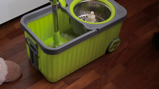 Green bucket and mop for cleaning and mopping the floor. Girl washes the floor at home. Modern mop for cleaning.