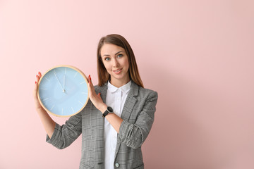 Young businesswoman with clock on color background