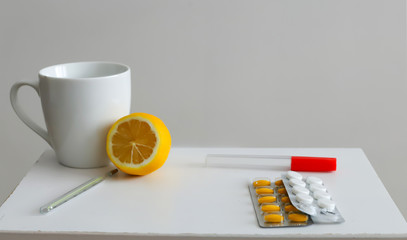 white mug on a wooden tray near lemon, honey and thermometer two kinds of pills on a white background concept illness, cold, flu
