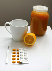 white mug on a wooden tray near lemon, honey and thermometer two kinds of pills on a white background concept illness, cold, flu