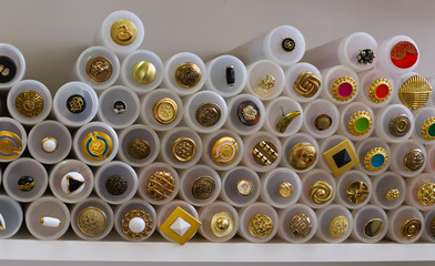 a large number of gold buttons with inserts of different colors in plastic containers on a white background concept of shop or factory of fabrics, handwork, knitting or embroidery