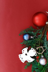 spruce branches with Christmas balls of different colors and a wooden angel on a red background in the corner place for text. concept new year and Christmas