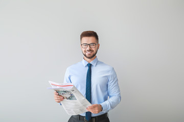 Handsome businessman with newspaper on light background