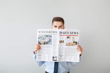 Handsome businessman with newspaper on light background