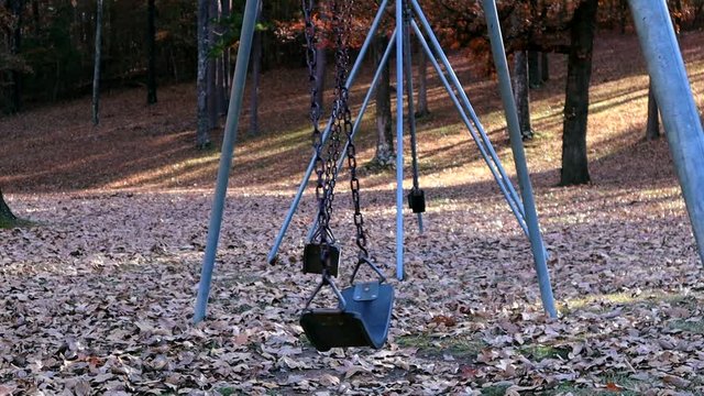Empty playground swings sway in the breeze on an autumn afternoon.