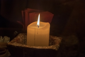 Big candle in a plate on a wooden table. Interior lighting with candles. Romantic interior in the dark.