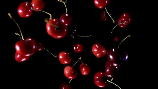 Close-up of juicy red cherry with sprigs bouncing up on black background