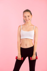 beautiful young woman with dumbbells in hands on pink background