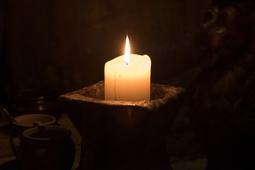 Big candle in a plate on a wooden table. Interior lighting with candles. Romantic interior in the dark.