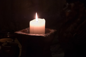 Big candle in a plate on a wooden table. Interior lighting with candles. Romantic interior in the dark.
