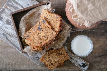 A glass of fresh milk, pieces of rye whole grain bread with prunes and dried apricots and a clay jug on the kitchen cutting board. View from the top.