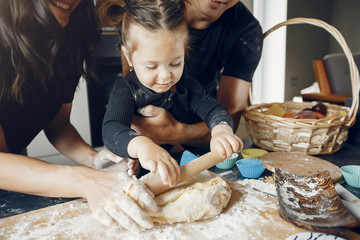 Family in a kitchen. Little girl with a dough. Mother and father in a black t-shirts