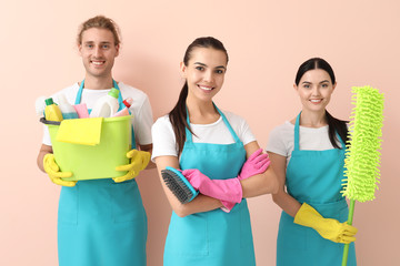 Team of janitors with cleaning supplies on color background