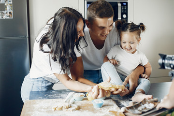 Fototapeta premium Family in a kitchen. Little girl with a dough. Mother and father in a white t-shirts