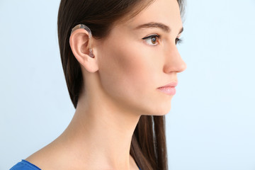Obraz premium Young woman with hearing aid on color background