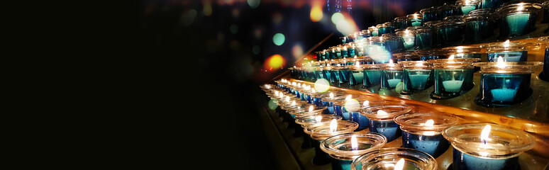 Candles in a church, cathedral or temple, in blue transparent candlesticks. The concept of mourning. We remember, we grieve. Selective focus, side view, copy space. Banner.