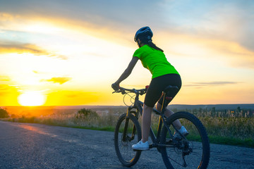 Fototapeta na wymiar Beautiful girl cyclist rides a bicycle on the road in the sunset. Healthy lifestyle and sport.