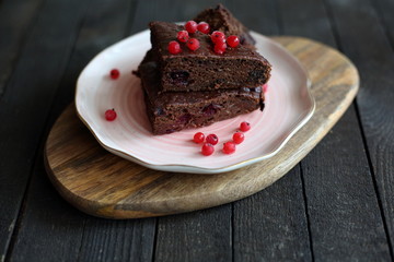 chocolate cake with prunes and cranberries on a dark wooden background.