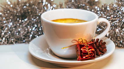 White hot cup of coffee with present, cone and tinsel. Concept of christmas drink on a white background.