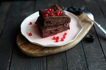 chocolate cake with prunes and cranberries on a dark wooden background.