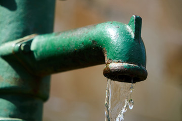 Water fountain releasing water through a pipe in a city. Metal fountain painted in green and antique look.