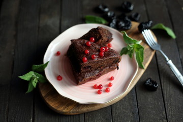 chocolate cake with prunes and cranberries on a dark wooden background.