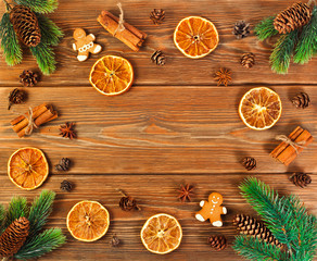 Christmas or New Year background. Fir branches, fir cones, dried orange slices, spices and gingerbread man on rustic wooden background. Top view. Text space.