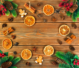 Christmas or New Year background. Fir branches, christmas wreath, red berries, fir cones, dried orange slices, spices and gingerbread man on rustic wooden background. Top view. Text space.