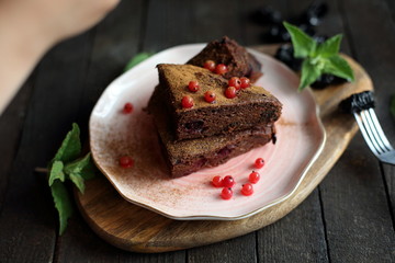 chocolate cake with prunes and cranberries on a dark wooden background.