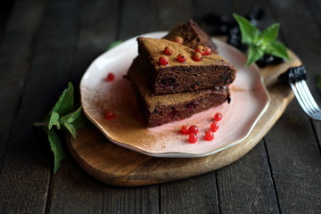 chocolate cake with prunes and cranberries on a dark wooden background.