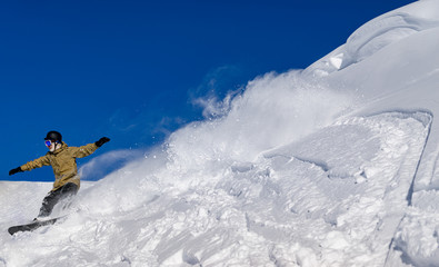Fototapeta na wymiar Freerider snowboarder moving down the slope in the mountains at high speed in snow powder