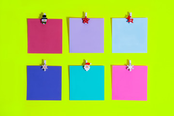Top view colorful reminder paper notes attached on a trendy bright light green background with christmas decorative pins. Festive planning concept. Gift, to do list. Minimalistic flat lay. Copy space.