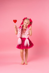 little girl with braids of pink kanekalon holds a heart-shaped Lollipop on a pink background. refusal of sweets. the concept of Valentine's day