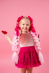 little girl with braids of pink kanekalon holds a heart-shaped Lollipop on a pink background. refusal of sweets. the concept of Valentine's day