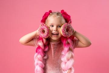cute little girl in a pink dress with pink braids from kanekalon holds donuts in pink glaze in her hands