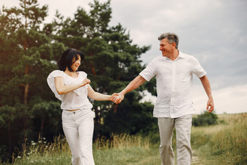 Fototapeta na wymiar Adult couple in a summer field. Handsome senior in a white shirt. Woman in a white blouse
