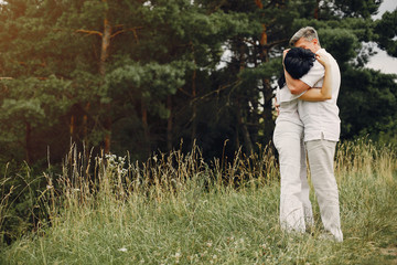 Adult couple in a summer field. Handsome senior in a white shirt. Woman in a white blouse