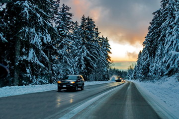 The icy Winter Road to the ski slopes of Seymour Mountains passes through a snowy forest, cars and...