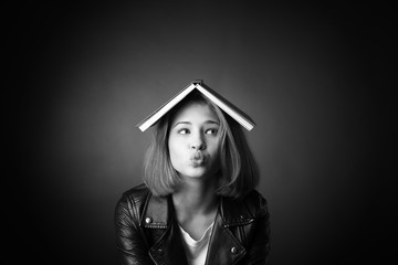Black and white portrait of funny teenage girl with book on dark background