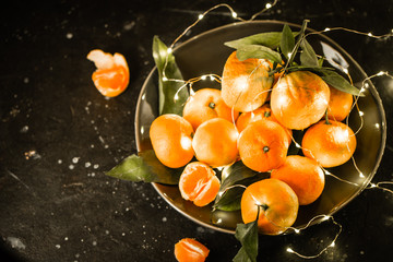 Tangerines or clementines in grey plate with bokeh lights in Christmas or New year arrangement,...