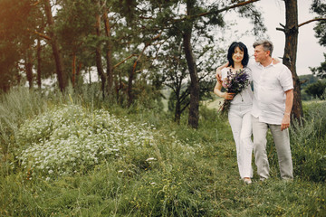 Adult couple in a summer field. Handsome senior in a white shirt. Woman in a white blouse